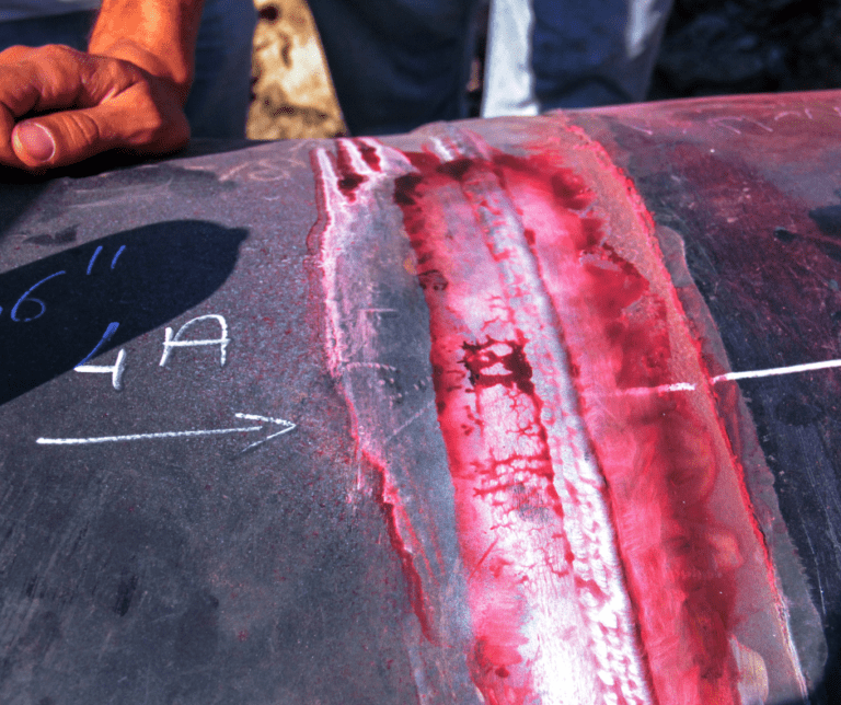 Penetrant inspection being conducted on a large pipe with red dye.
